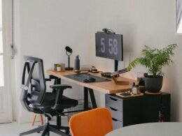 Ein Schreibtisch mit Computer und Stuhl steht in einem hellen, modern gestalteten Arbeitszimmer