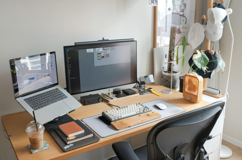 Ein Schreibtisch mit einem aufgeklappten Laptop und einem großen Computer-Monitor, ideal für produktives Arbeiten.
