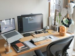 Ein moderner Schreibtisch mit einem aufgeklappten Laptop und einem danebenstehenden Monitor in einem hellen Raum.