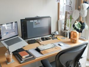 Ein Schreibtisch mit einem geöffneten Laptop und einem großen Computerbildschirm in einem modernen Arbeitsumfeld