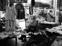 Schwarzweißfoto eines Mannes, der in einem Geschäft an einem Tisch sitzt, aufgenommen aus mittlerer Distanz