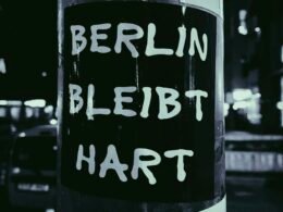 Schwarz-Weiß-Foto eines Schilds, das an einem Metallpfosten befestigt ist, aufgenommen im städtischen Umfeld