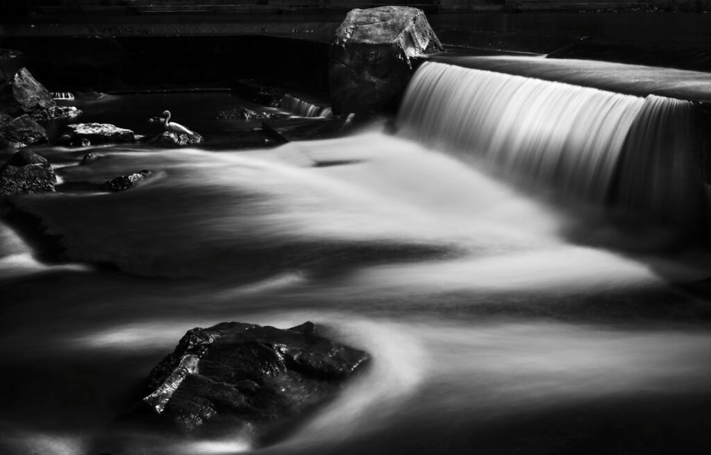 Schwarz-weißes Foto eines Wasserfalls mit hervorgehobenen Strukturen und fließendem Wasser im Vordergrund