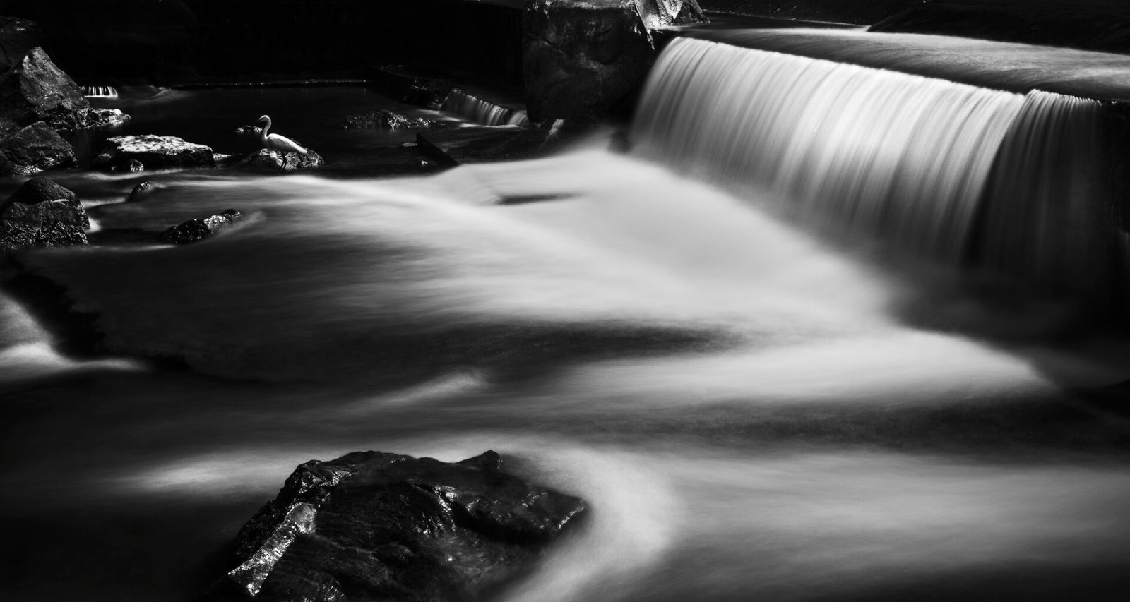 Schwarz-weißes Foto eines Wasserfalls mit hervorgehobenen Strukturen und fließendem Wasser im Vordergrund