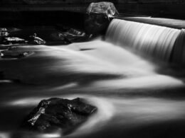 Schwarz-weißes Foto eines Wasserfalls mit hervorgehobenen Strukturen und fließendem Wasser im Vordergrund