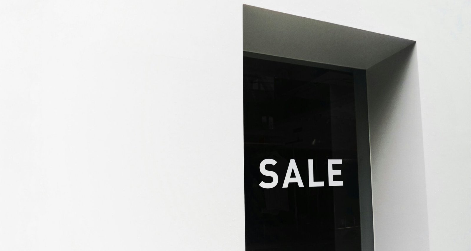 Schwarz-weißes Sale-Schild auf weißer Wand, geeignet für Beiträge zu Einzelhandel, Marketing oder Verkaufsaktionen.