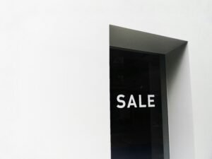 Schwarz-weißes Sale-Schild auf weißer Wand, geeignet für Beiträge zu Einzelhandel, Marketing oder Verkaufsaktionen.