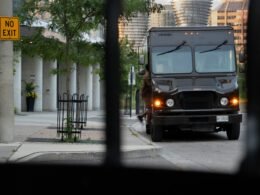 Schwarzer LKW fährt auf einer Straße entlang, flankiert von hohen Gebäuden im Hintergrund