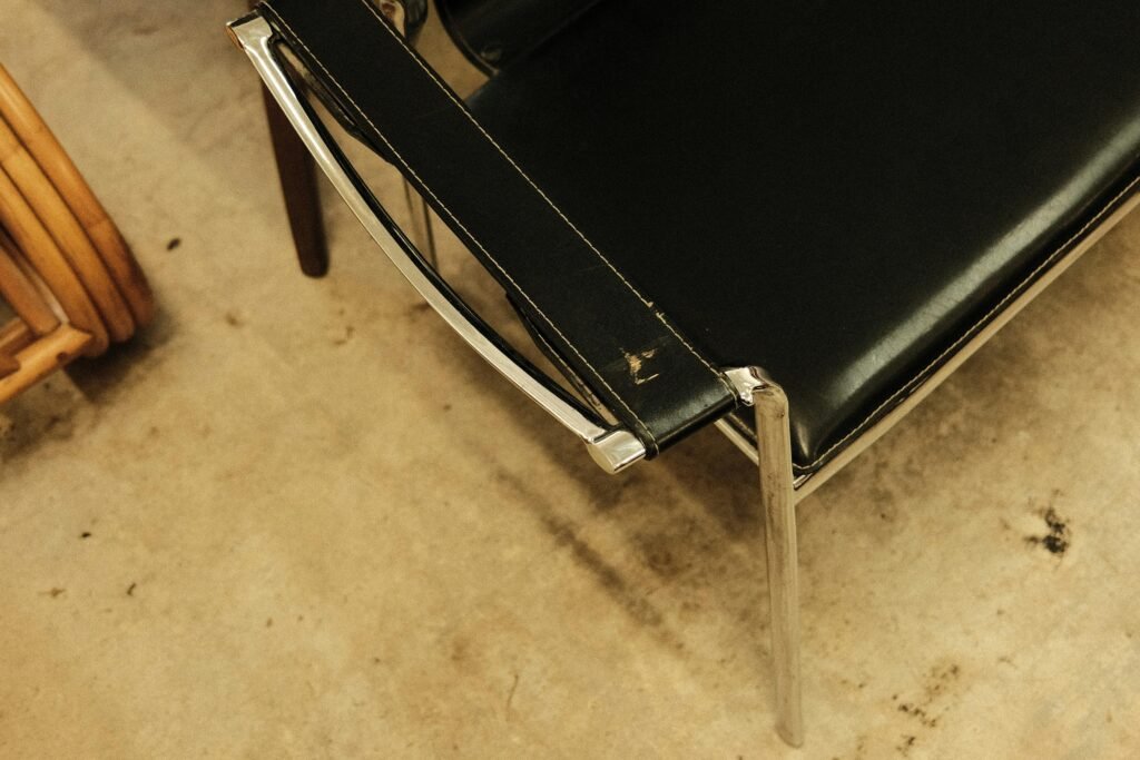 Ein schwarzer Lederstuhl steht direkt neben einem Holzstuhl auf einem schlichten Boden, beide sind leer und gut beleuchtet.