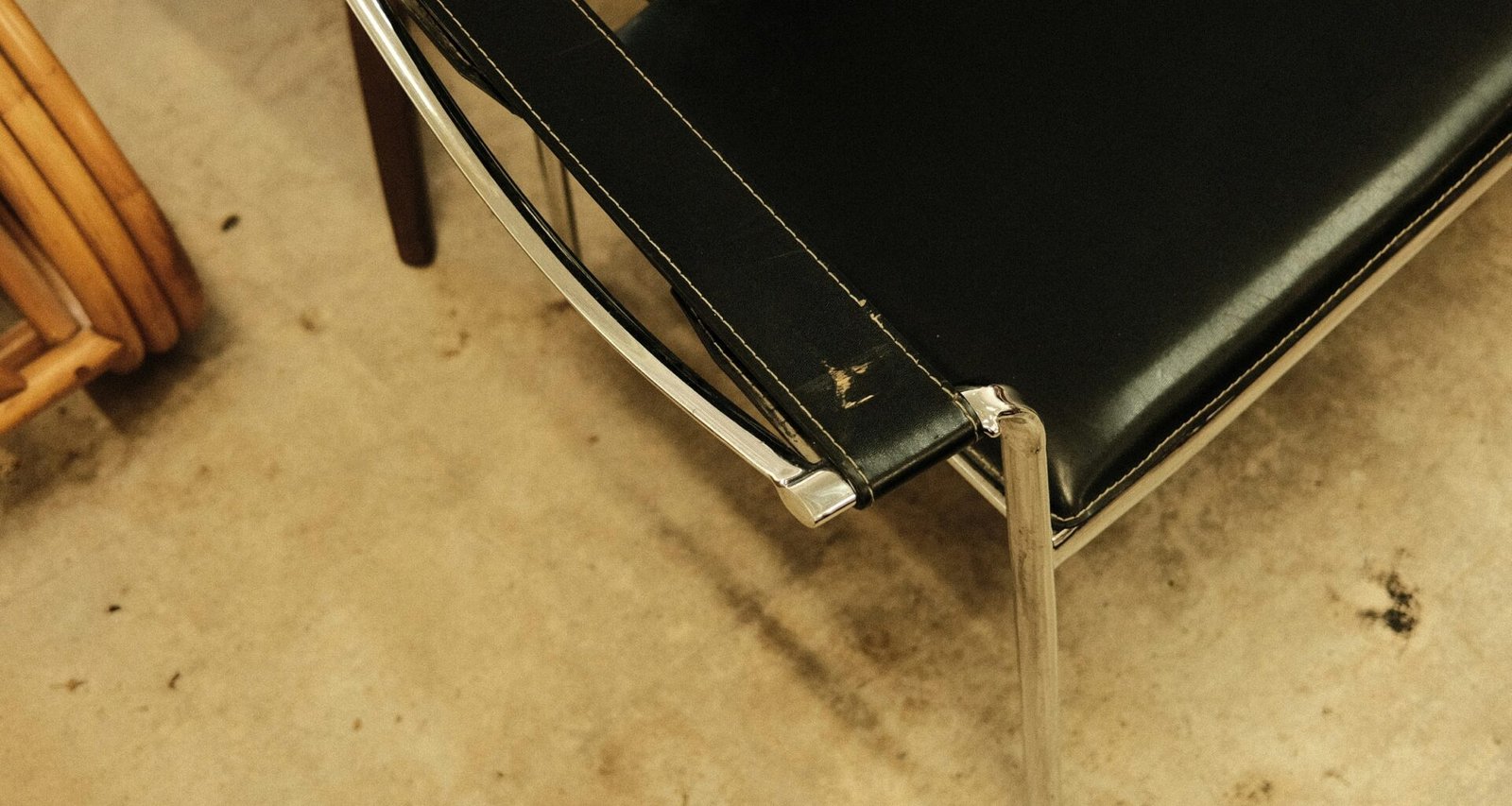 Ein schwarzer Lederstuhl steht direkt neben einem Holzstuhl auf einem schlichten Boden, beide sind leer und gut beleuchtet.