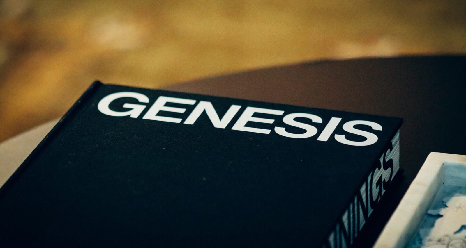 Schwarzes Buch mit dem Wort Genesis auf dem Umschlag, auf einer neutralen Oberfläche liegend, fotografiert von Jon Tyson