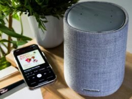 Ein Smartphone ist über ein Kabel mit einem zylinderförmigen Lautsprecher verbunden, moderner Technik-Hintergrund.