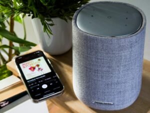 Ein Smartphone ist über ein Kabel mit einem zylinderförmigen Lautsprecher verbunden, moderner Technik-Hintergrund.