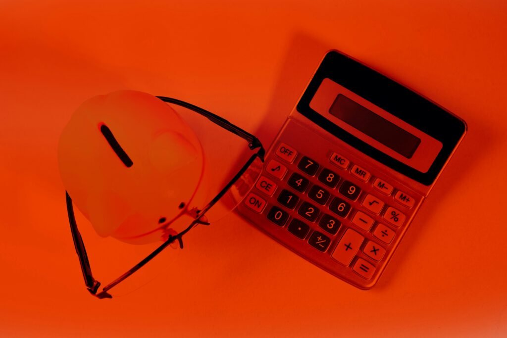 Ein rosa Sparschwein und ein schwarzer Taschenrechner nebeneinander auf einer orangefarbenen Fläche