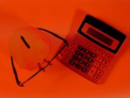 Sparschwein und Taschenrechner liegen auf orangefarbenem Hintergrund als Symbol für Finanzplanung und Kostenkontrolle.