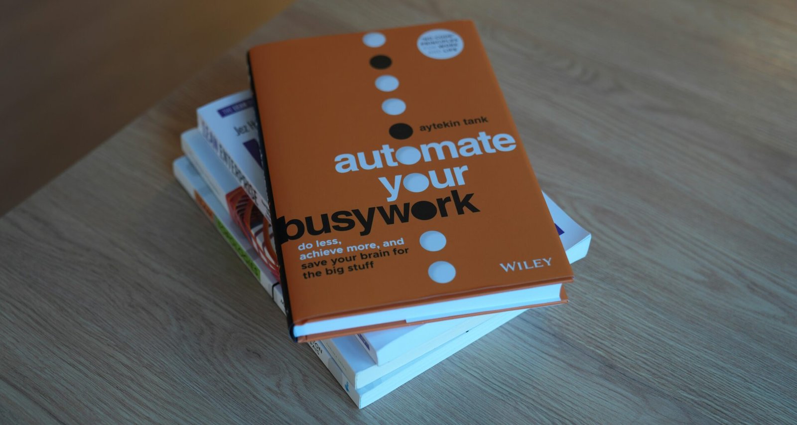 Ein ordentlicher Stapel Bücher liegt auf einem hellen Holztisch in ruhiger Atmosphäre, ideales Setting für Recherchen und Lernen.