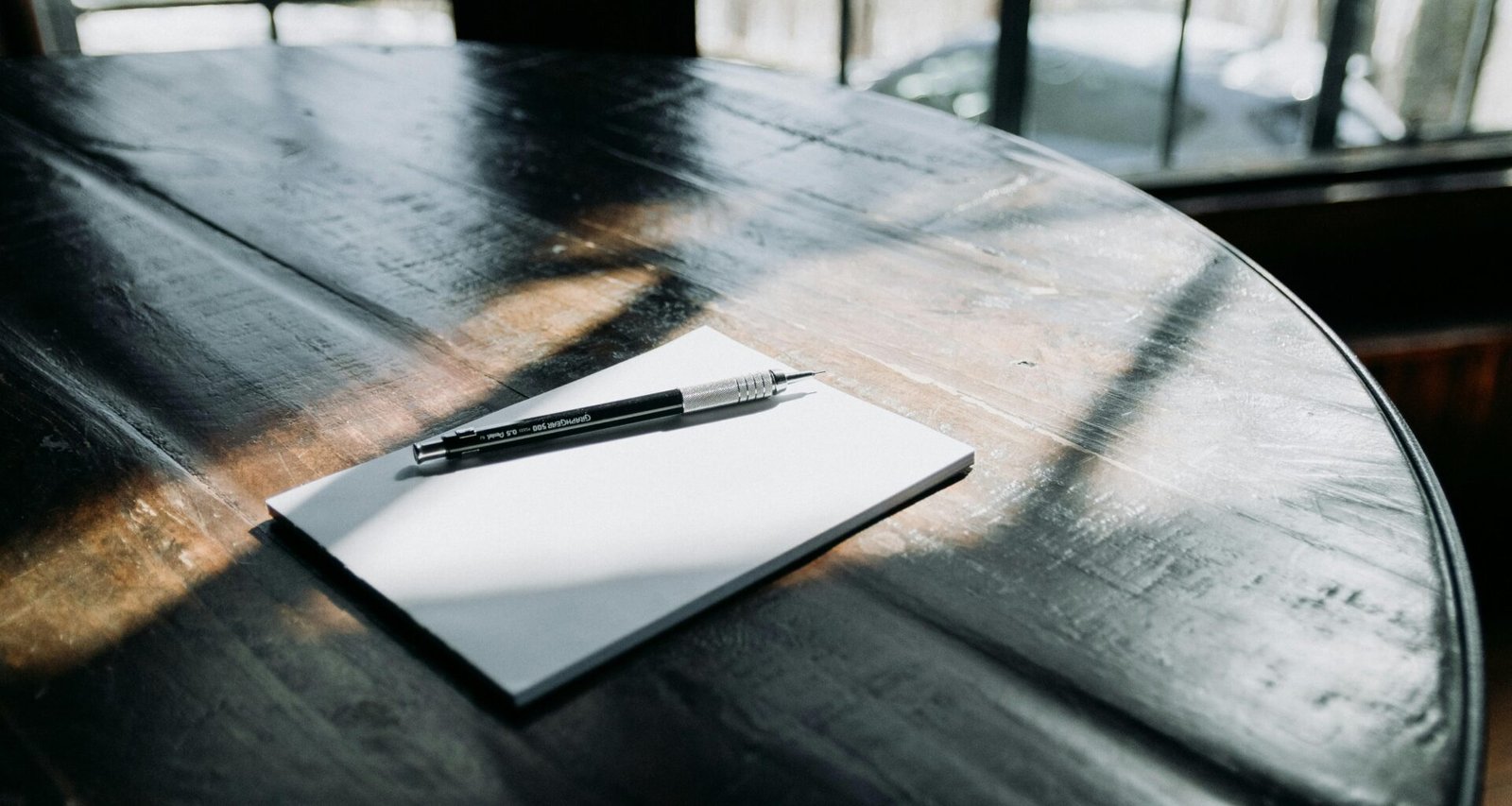 Ein Kugelschreiber liegt auf einem weißen Blatt Papier auf einem Holztisch, bereit für Notizen oder Skizzen.