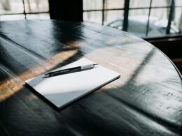 Ein Kugelschreiber liegt auf einem weißen Blatt Papier auf einem Holztisch, bereit für Notizen oder Skizzen.