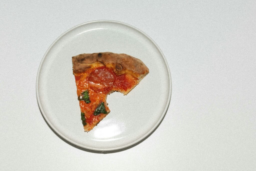 Eine einzelne Pizzascheibe auf einem weißen Teller, platziert auf einem Holztisch, aus der Vogelperspektive fotografiert