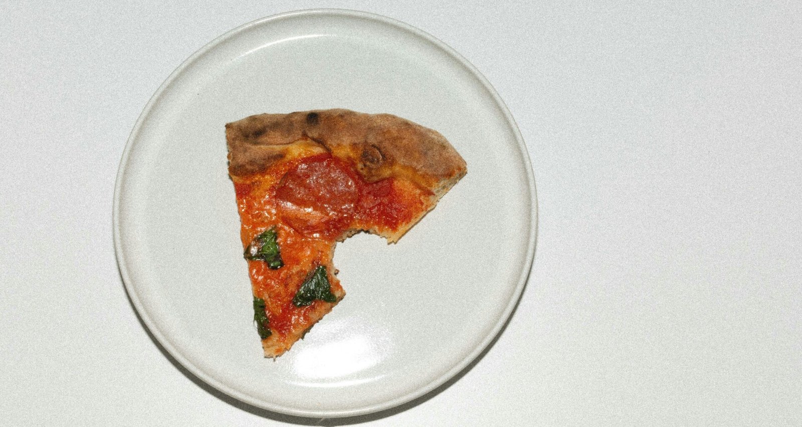 Eine einzelne Pizzascheibe auf einem weißen Teller, platziert auf einem Holztisch, aus der Vogelperspektive fotografiert