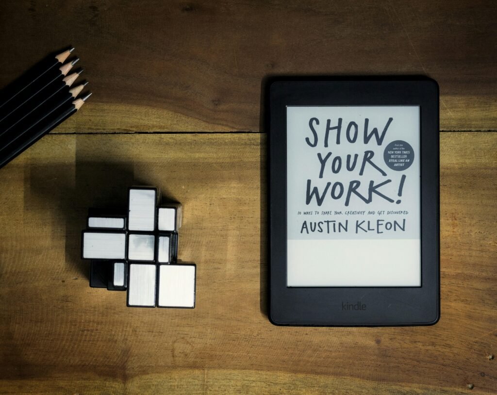 Tablet mit aufgeschlagenem Buch 'Show Your Work' auf einem hellen Untergrund, geeignet für Online-Marketing-Artikel