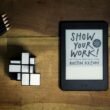 Tablet mit aufgeschlagenem Buch 'Show Your Work' auf einem hellen Untergrund, geeignet für Online-Marketing-Artikel