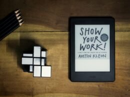 Tablet mit aufgeschlagenem Buch 'Show Your Work' auf einem hellen Untergrund, geeignet für Online-Marketing-Artikel