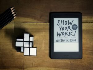 Tablet mit aufgeschlagenem Buch 'Show Your Work' auf einem hellen Untergrund, geeignet für Online-Marketing-Artikel