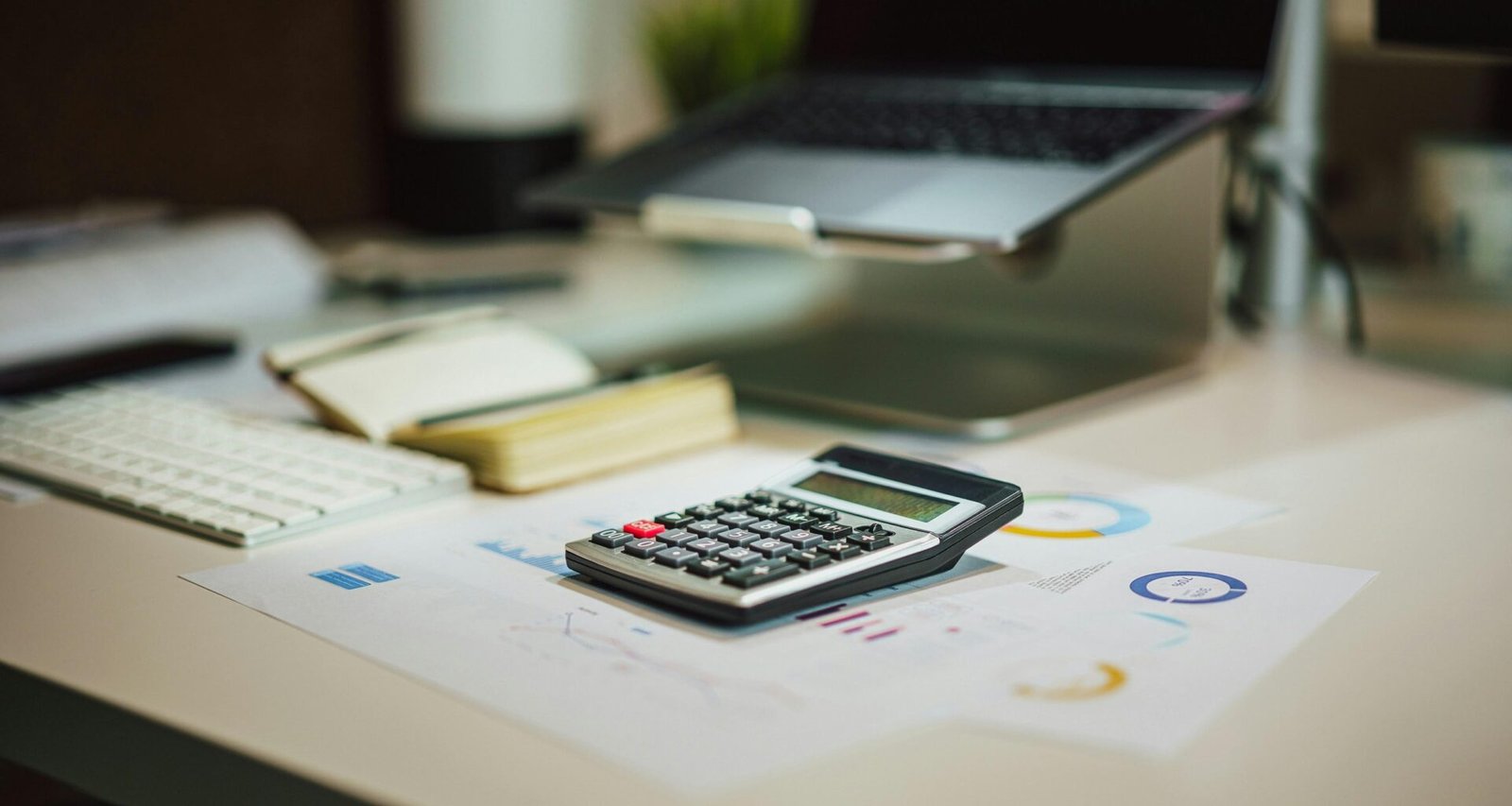 Ein Taschenrechner liegt auf einem Holztisch direkt neben einem aufgeklappten Laptop – moderne Arbeitsumgebung.