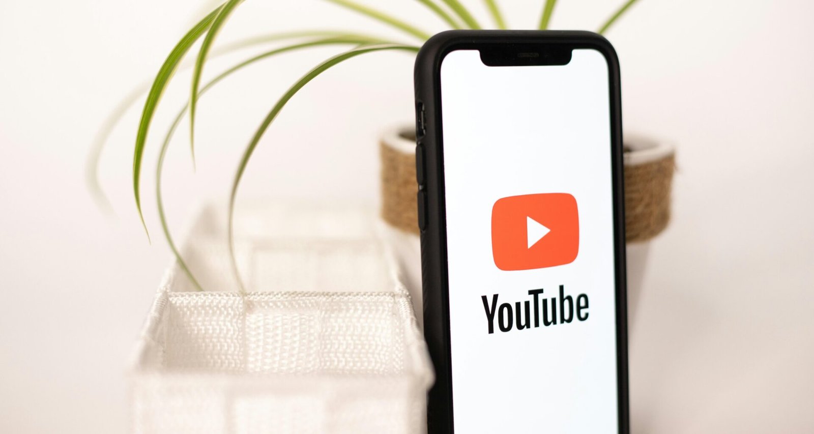 Ein Smartphone mit YouTube-Logo liegt auf einem Tisch neben einer kleinen Topfpflanze, Symbol für digitales Mediennutzung.