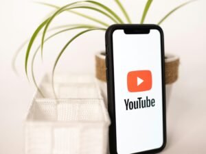 Ein Smartphone mit YouTube-Logo liegt auf einem Tisch neben einer kleinen Topfpflanze, Symbol für digitales Mediennutzung.