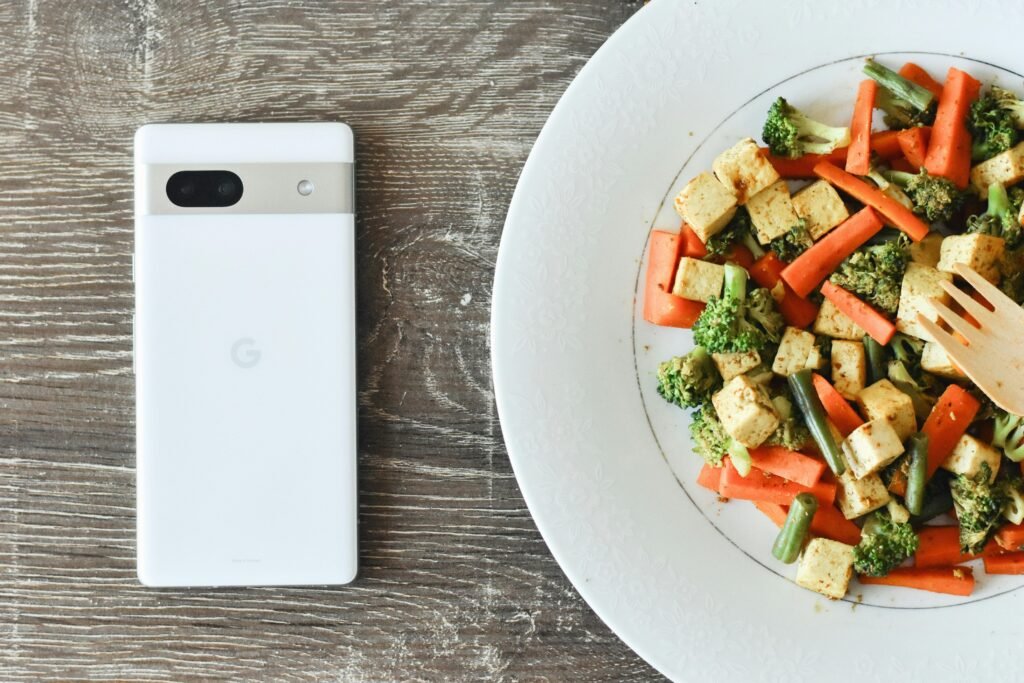 Ein Teller mit einer Mahlzeit, daneben liegt ein Smartphone auf einem Tisch in moderner Umgebung.