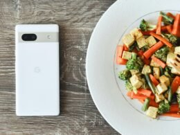 Ein Teller mit einer Mahlzeit, daneben liegt ein Smartphone auf einem Tisch in moderner Umgebung.
