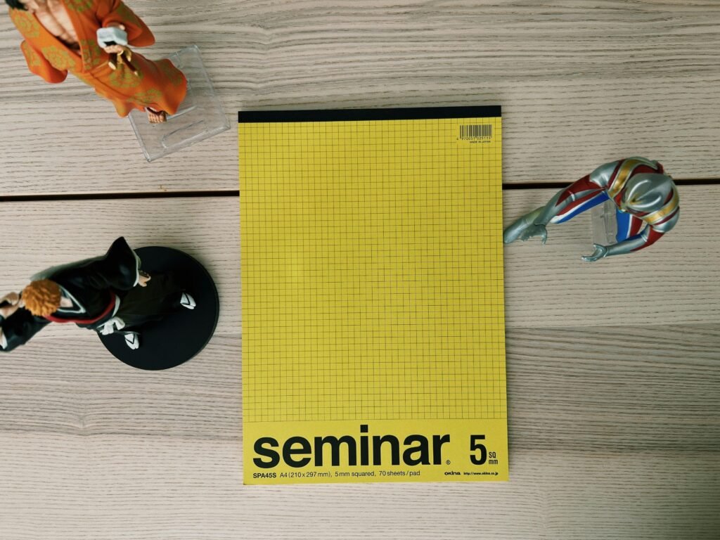 Ein gelbes Buch und eine silberne Schere liegen nebeneinander auf einem hellen Holztisch