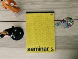 Ein gelbes Buch und eine silberne Schere liegen nebeneinander auf einem hellen Holztisch