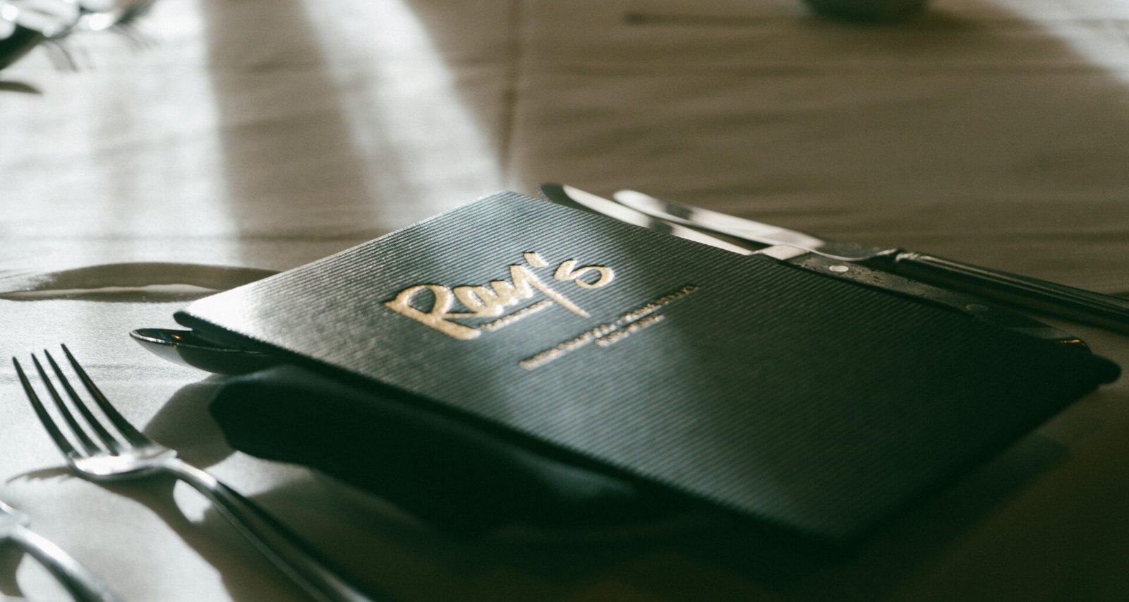 Ein Tisch mit Menükarte und silbernem Besteck, sorgfältig arrangiert für ein bevorstehendes Essen in einem modernen Ambiente.