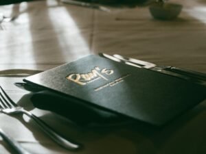 Ein Tisch mit Menükarte und silbernem Besteck, sorgfältig arrangiert für ein bevorstehendes Essen in einem modernen Ambiente.