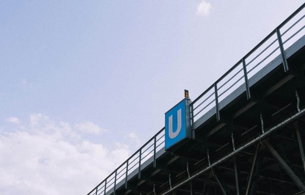 U-Bahn-Schild auf einer Brücke, fotografiert aus der Straßenperspektive mit Blick auf das leuchtende blaue Zeichen