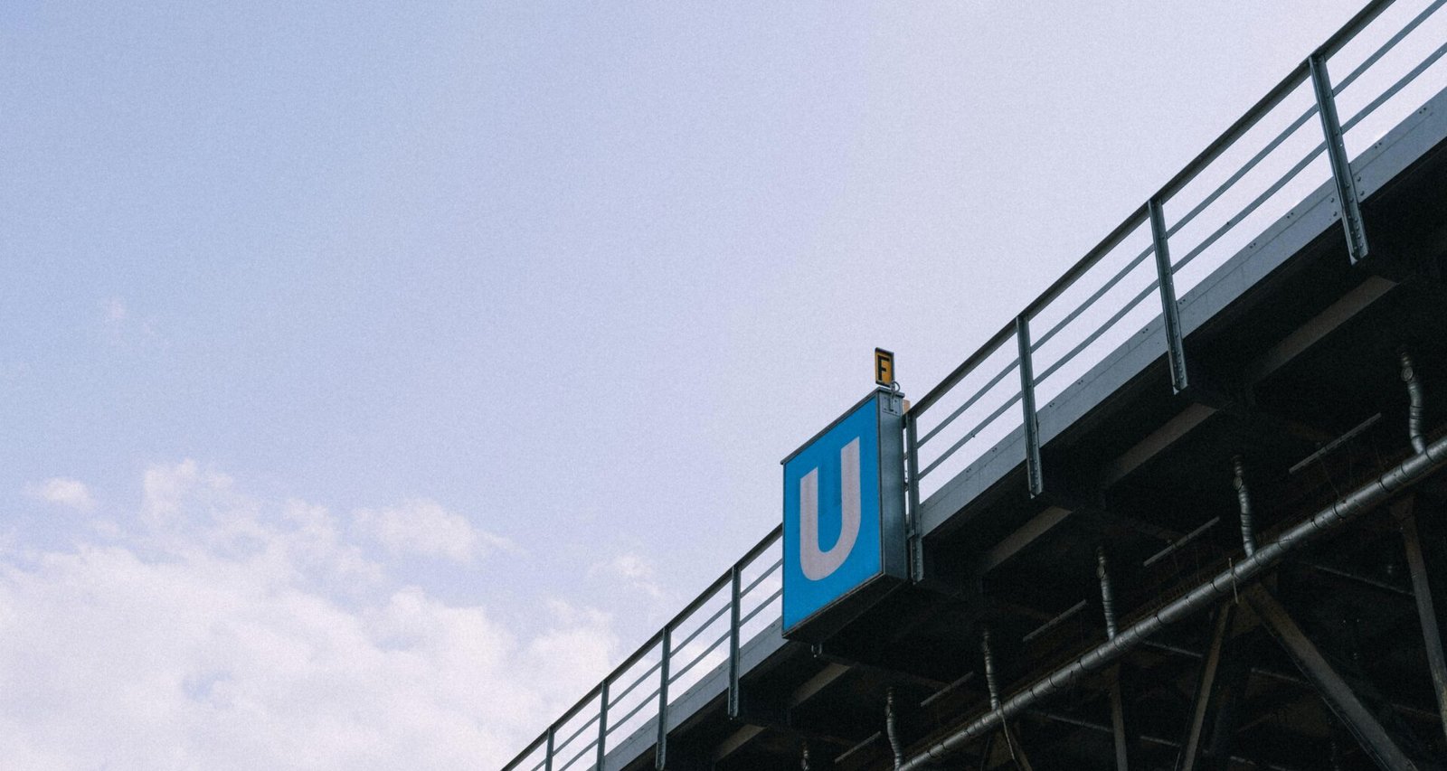 U-Bahn-Schild auf einer Brücke, fotografiert aus der Straßenperspektive mit Blick auf das leuchtende blaue Zeichen