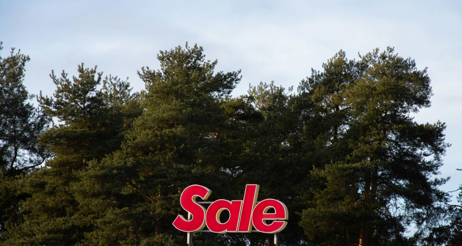 Ein großes Sale-Schild befindet sich auf dem Dach eines Gebäudes, im Hintergrund sind mehrere Bäume zu sehen