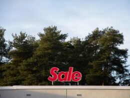 Ein großes Sale-Schild befindet sich auf dem Dach eines Gebäudes, im Hintergrund sind mehrere Bäume zu sehen