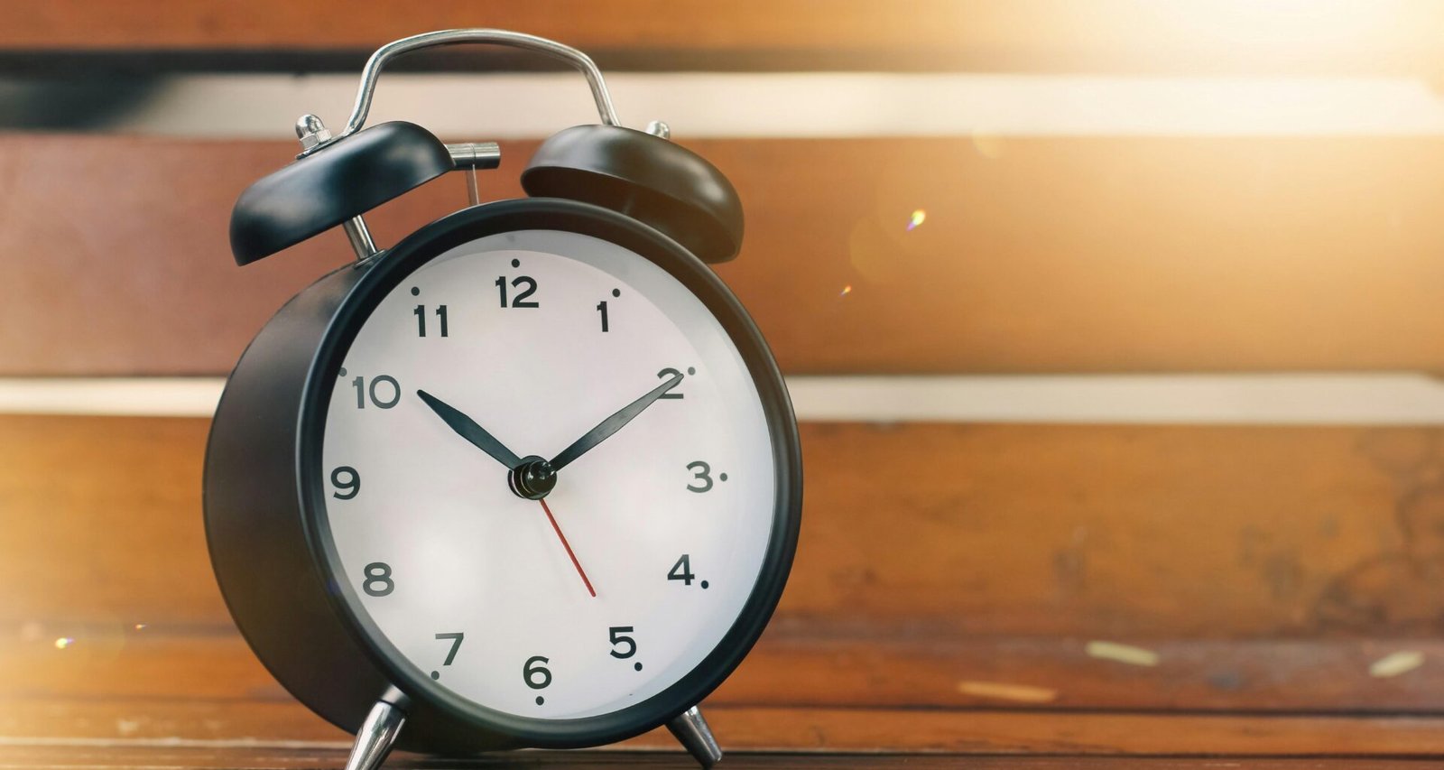 Ein klassischer, analoger Wecker steht auf einem Holzschreibtisch, fotografiert aus der Nähe in natürlichem Licht.