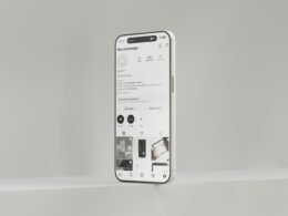 Ein weißes Mobiltelefon hängt mittig an einer hellen Wand, minimalistisches Motiv, Technik-Symbolbild