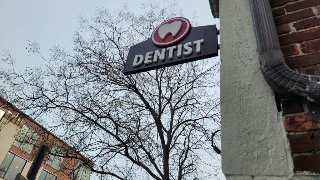 Ein Zahnarzt-Schild hängt an der Fassade eines Gebäudes und zeigt den Standort einer Zahnarztpraxis in der Stadt an.