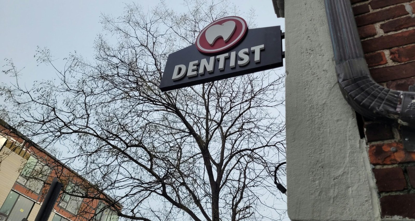 Ein Zahnarzt-Schild hängt an der Fassade eines Gebäudes und zeigt den Standort einer Zahnarztpraxis in der Stadt an.
