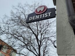 Ein Zahnarzt-Schild hängt an der Fassade eines Gebäudes und zeigt den Standort einer Zahnarztpraxis in der Stadt an.