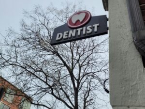 Ein Zahnarzt-Schild hängt an der Fassade eines Gebäudes und zeigt den Standort einer Zahnarztpraxis in der Stadt an.