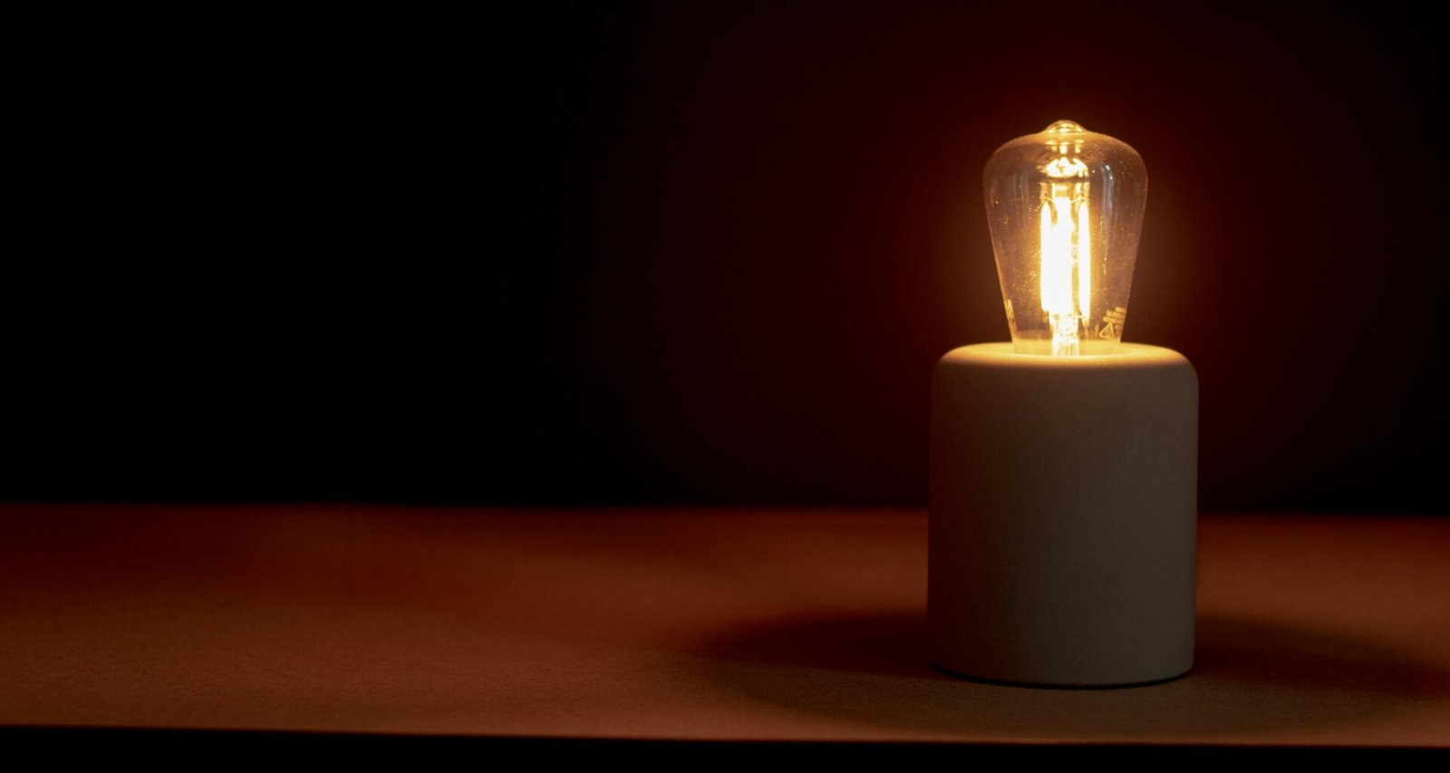 Eine einzelne brennende Kerze steht in einem dunklen Raum und spendet warmes Licht auf einer ebenen Fläche.