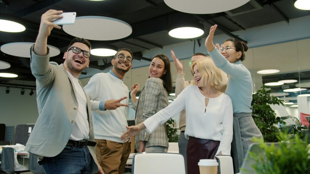 Eine Gruppe von Kollegen unterschiedlicher Herkunft macht ein gemeinsames Selfie in einem modernen Büro an einem Arbeitstag.
