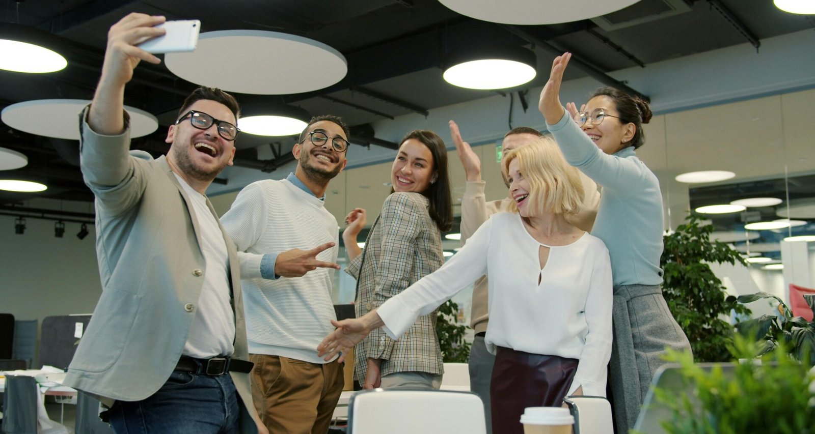 Eine Gruppe von Kollegen unterschiedlicher Herkunft macht ein gemeinsames Selfie in einem modernen Büro an einem Arbeitstag.